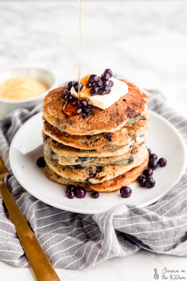 A stack of vegan blueberry pancakes with syrup and blueberries.