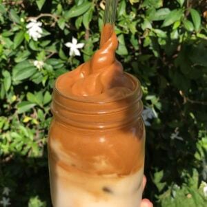 Whipped coffee in a mason jar being twirled out with a straw.
