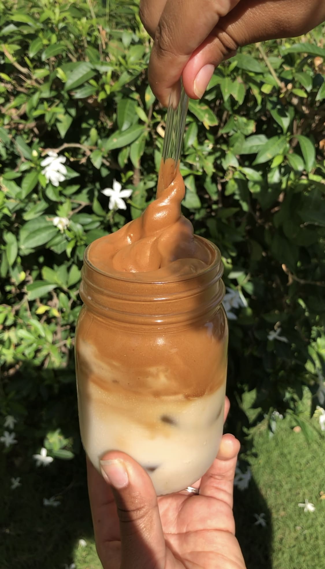 Whipped coffee in a mason jar being twirled out with a glass straw.