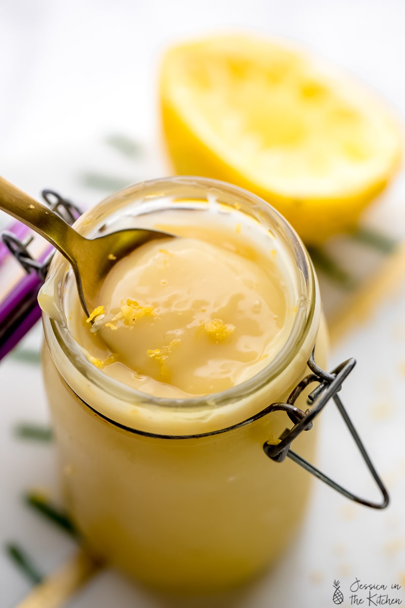Close up of a spoon scooping out vegan lemon curd from a glass.