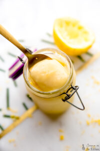 A gold spoon scooping out vegan lemon curd from a little glass jar.