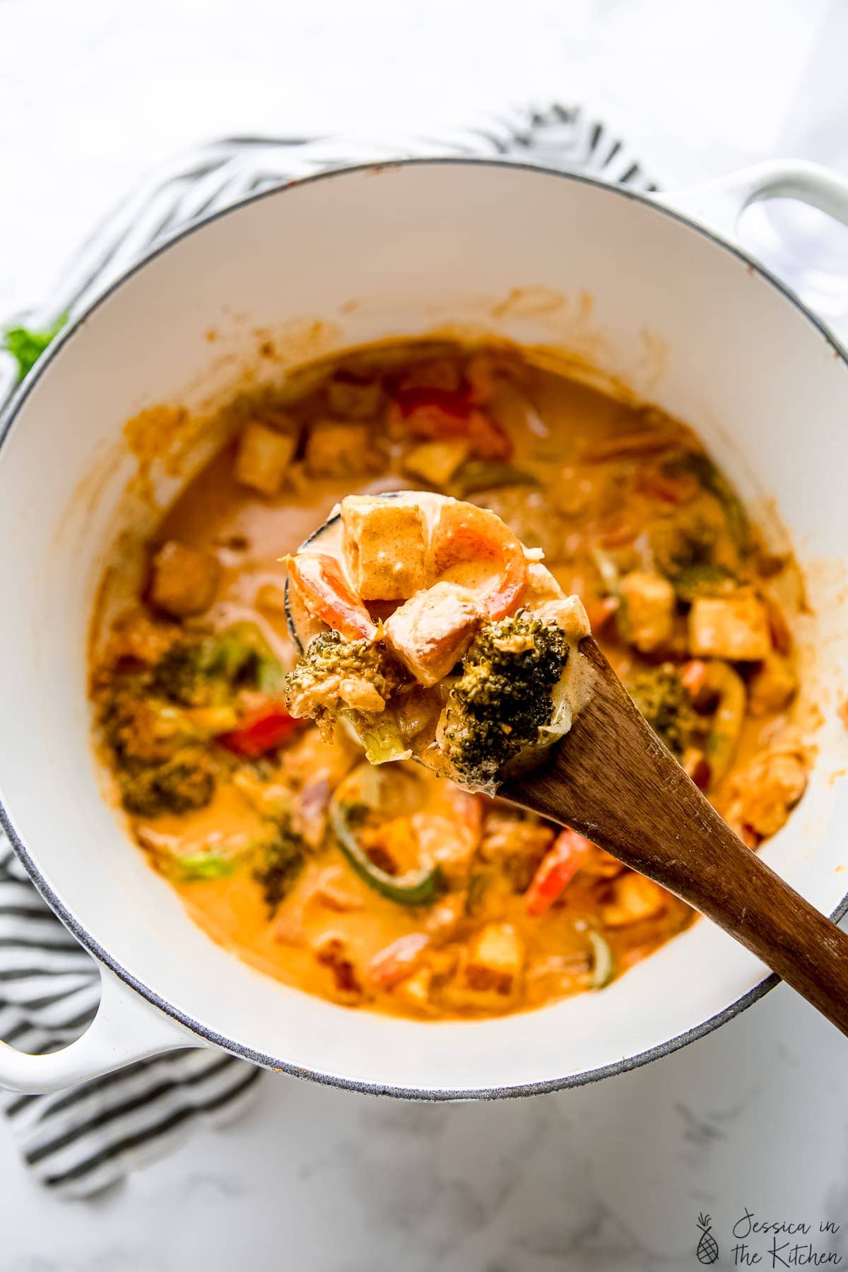 Wooden spoon holding Thai red curry over Dutch oven