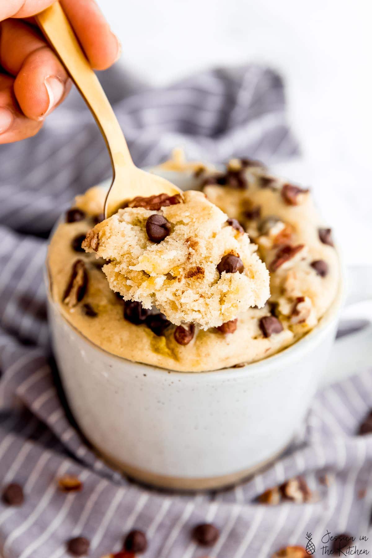 A spoon of banana bread mug cake in front of a mug with banana bread mug cake.