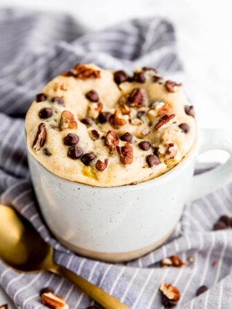 Banana bread mug cake in a mug with a golden spoon in front.