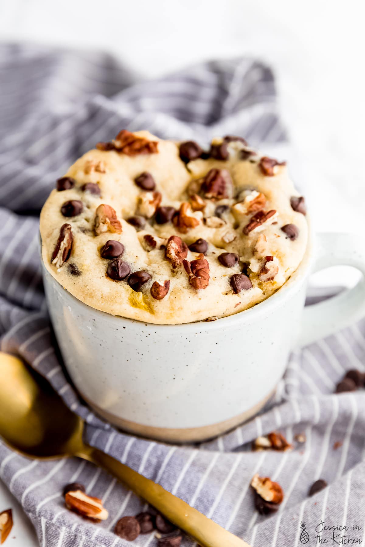 A banana bread mug cake in a coffee mug with a golden spoon in front.