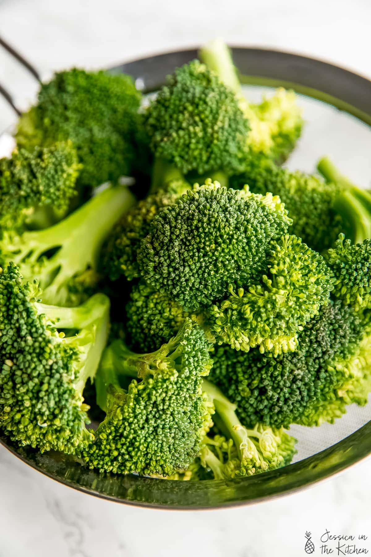 Close up shot of raw broccoli in a metal strainer.