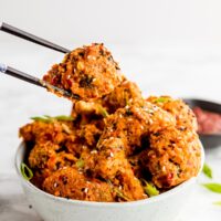 Bang bang broccoli being held by chopsticks over a bowl with more broccoli in it.