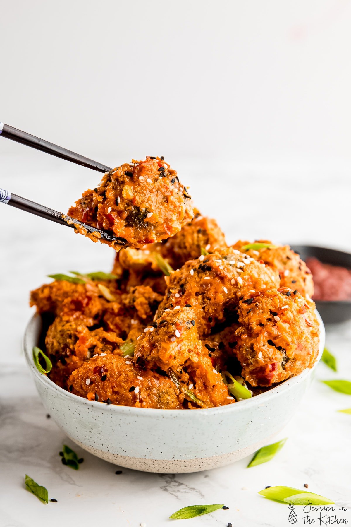 Bang bang broccoli being held by chopsticks over a bowl with more bang bang broccoli in it.