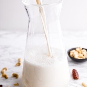 Cashew milk being poured into a glass jug.