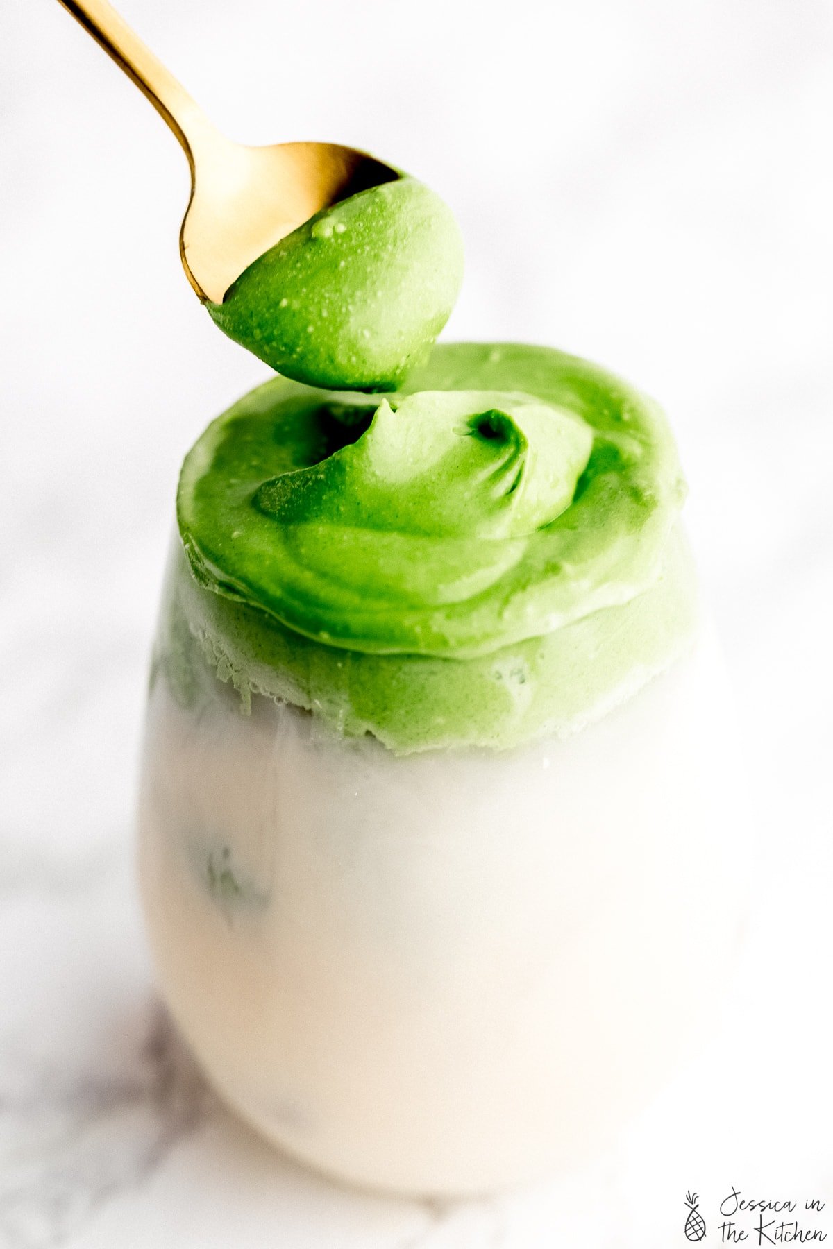 Whipped matcha in a glass with milk with a gold spoon pulling the whipped matcha froth.