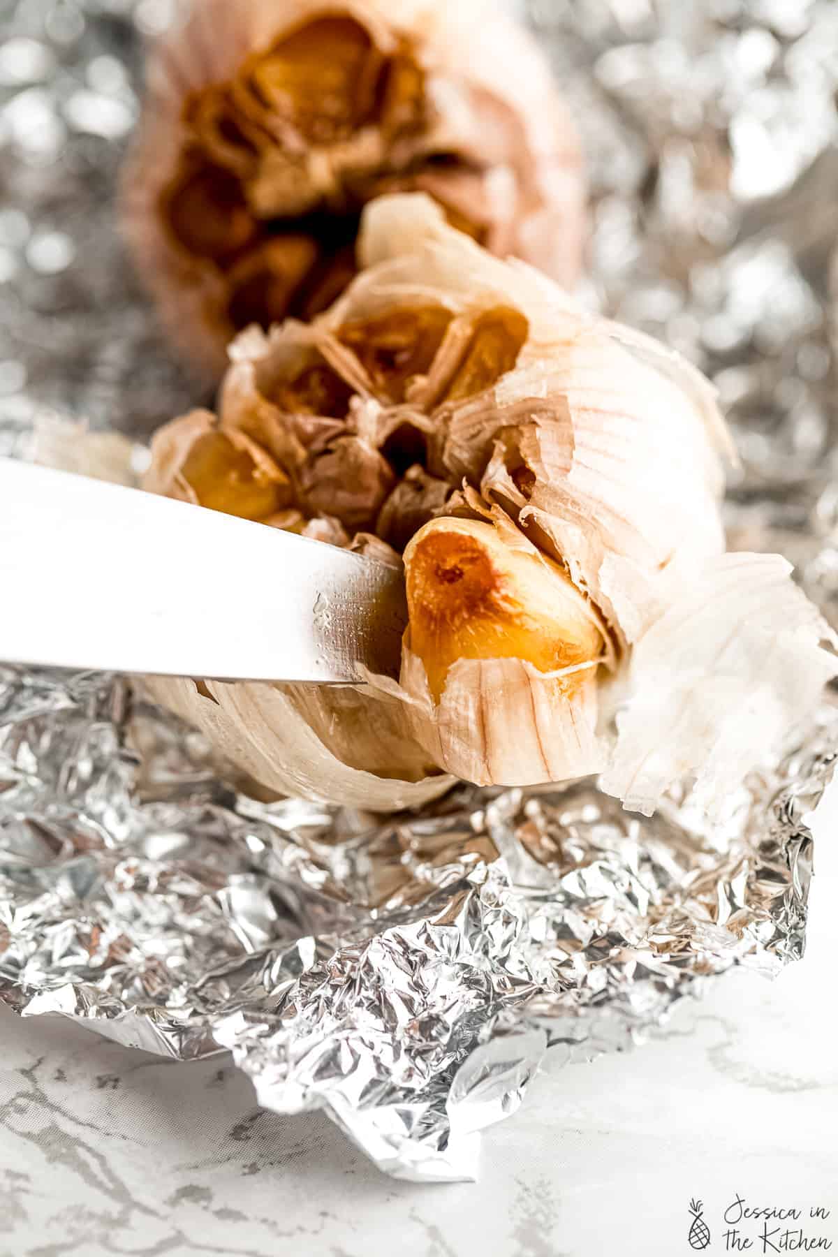 A knife slicing into a bulb of roasted garlic.