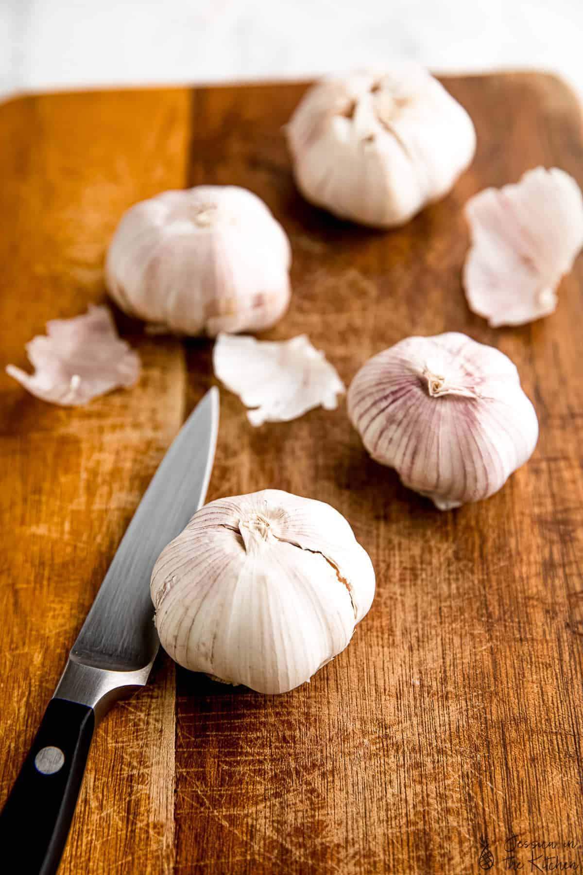 Bulbs of garlic on a wood board with a knife.