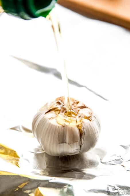 Olive oil poured onto a bulb of garlic.