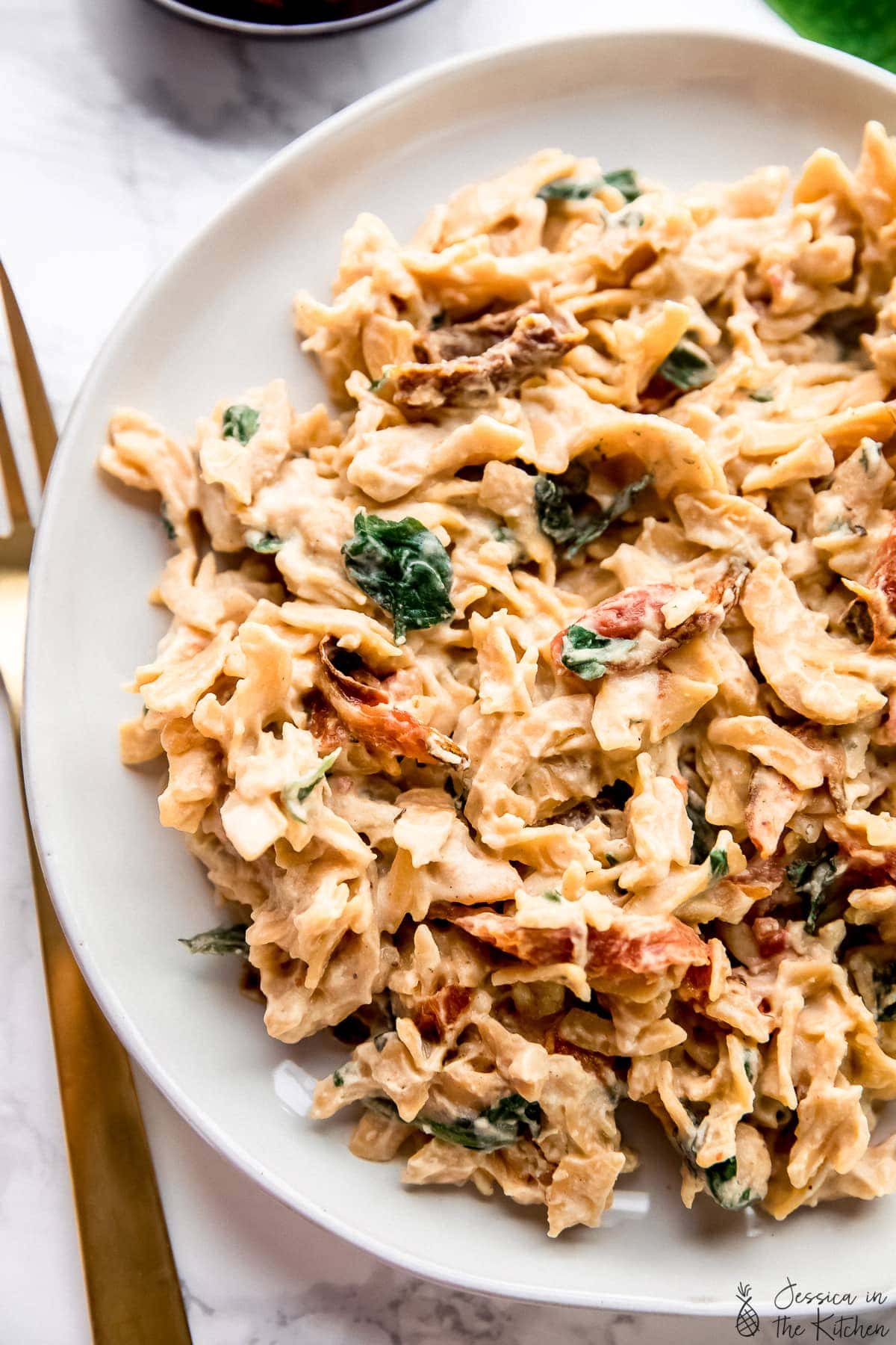 Pasta tossed with hummus, spinach, and sun dried tomatoes on a white plate