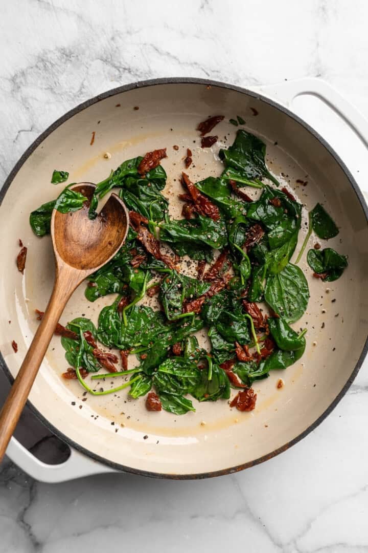 Wilted spinach and sun-dried tomatoes in skillet.