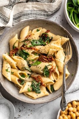 Bowl of hummus pasta with sun-dried tomatoes and spinach.