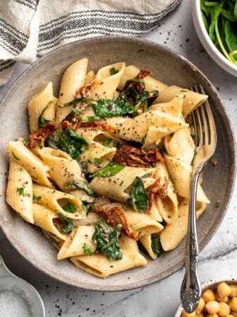Bowl of hummus pasta with sun-dried tomatoes and spinach.