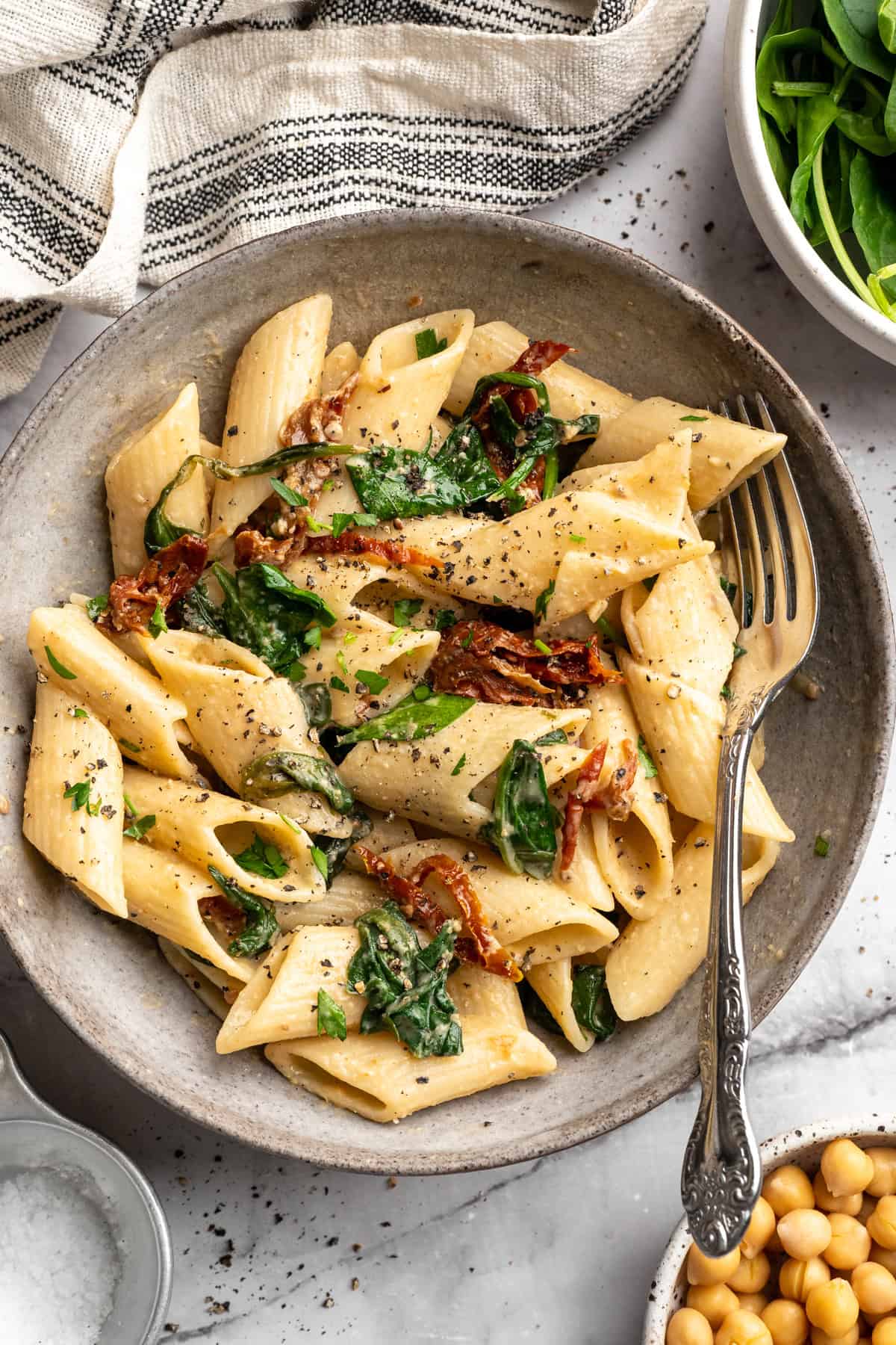 Bowl of hummus pasta with sun-dried tomatoes and spinach.