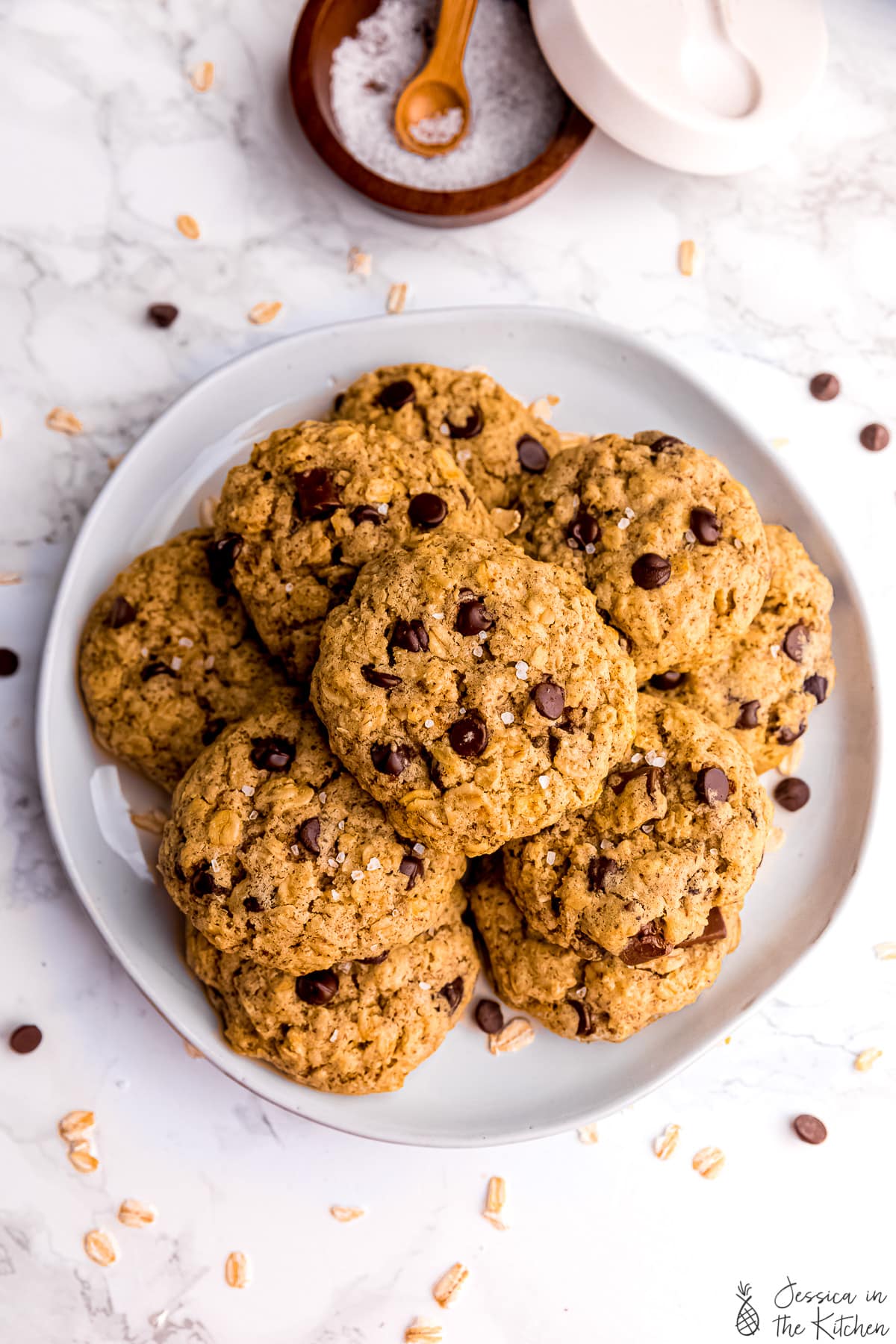 Top down view of oatmeal chocolate chip cookies on a plate with a pot of salt on the side. 