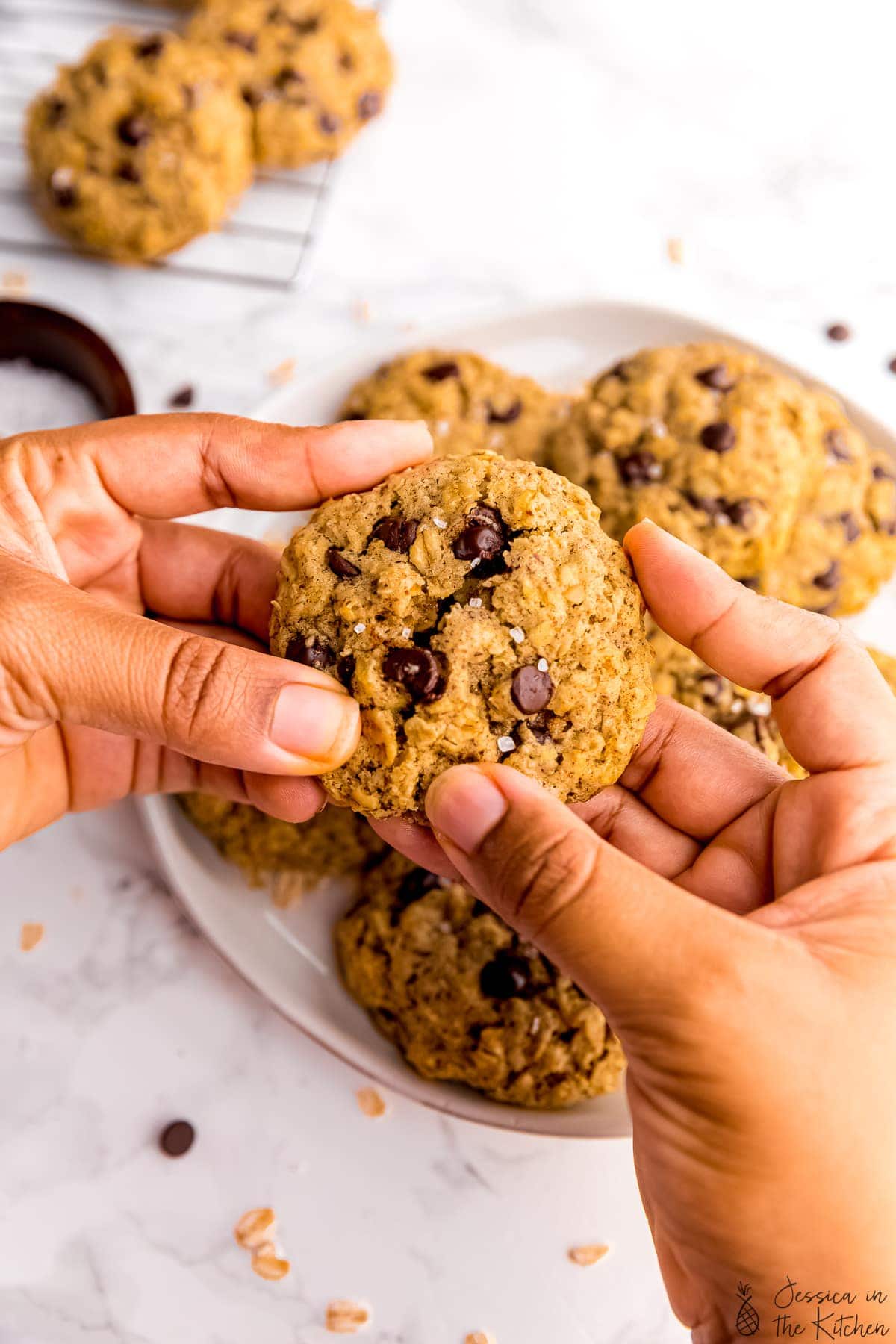 Hands breaking chewy oatmeal chocolate chip cookie in half