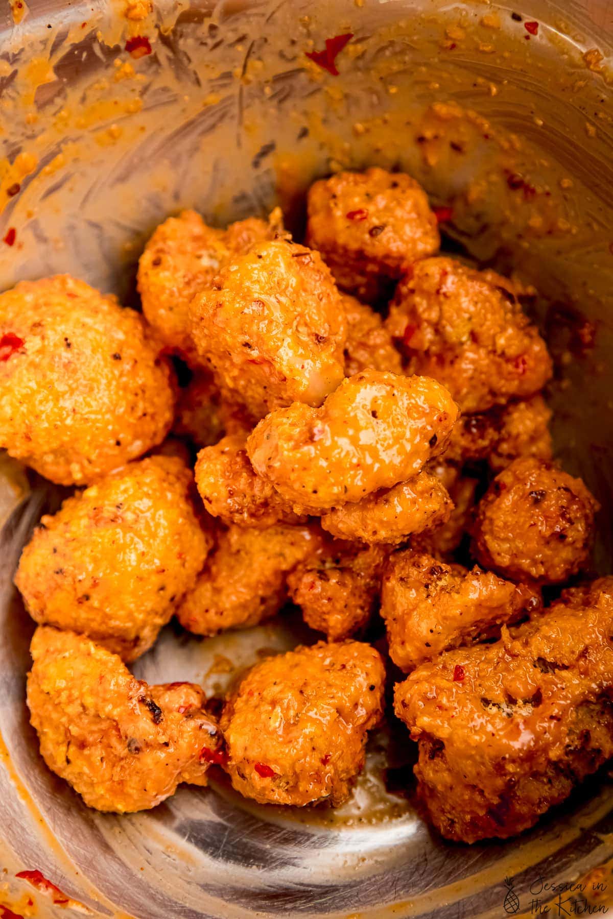 Baked cauliflower wings in a bowl with bang bang sauce covering the wings.