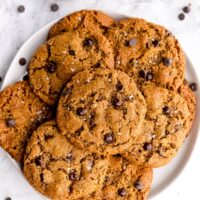 Five ingredient chocolate chip cookies stacked on each other on a plate in front of a jar of salt