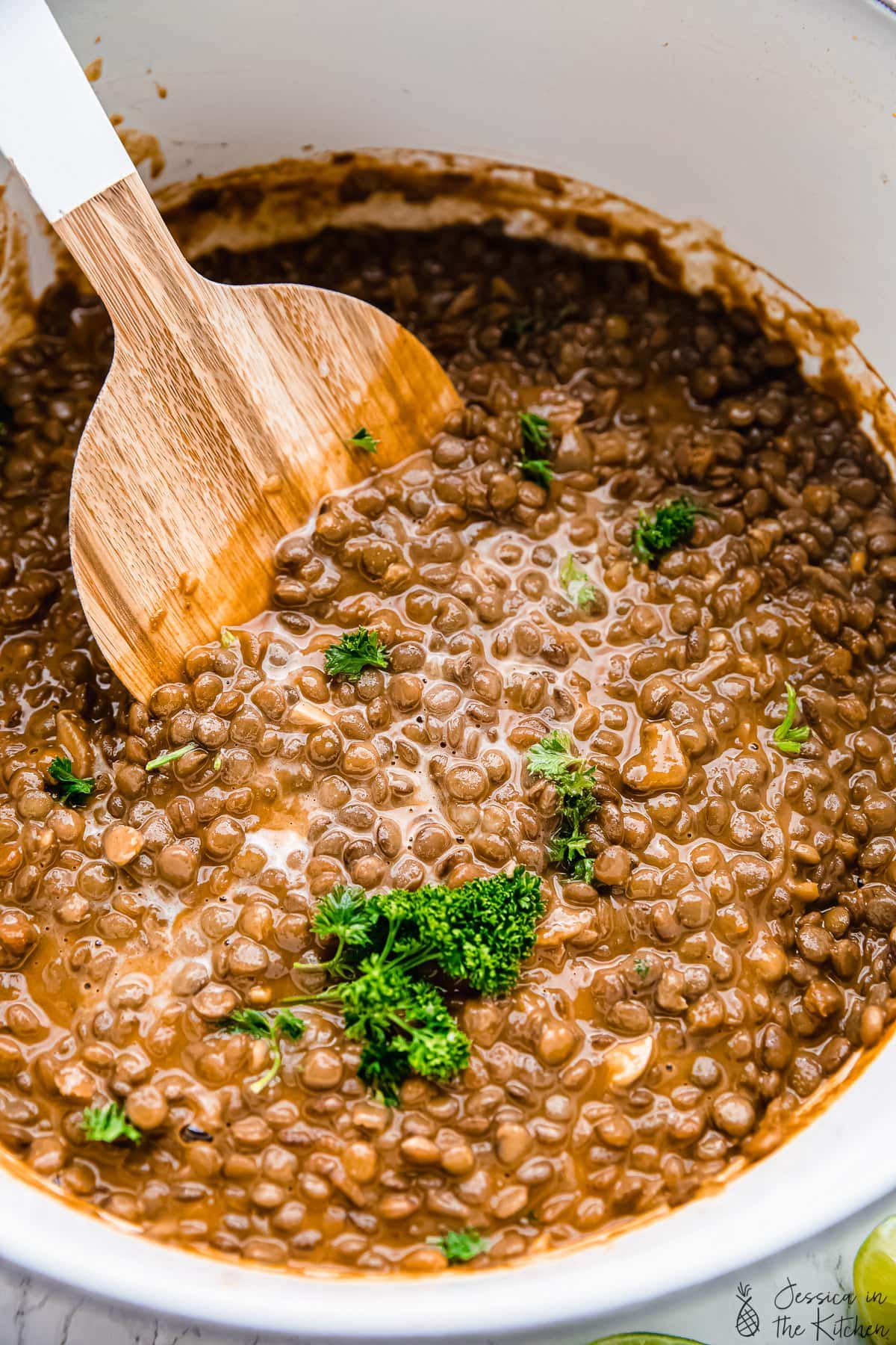 A large wood spoon stirring vegan lentil stew.