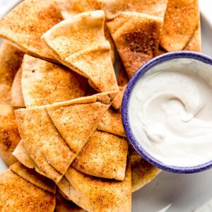 Homemade pita chips in a plate stacked with a dip beside it.