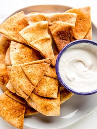 Homemade pita chips in a plate stacked with a dip beside it.