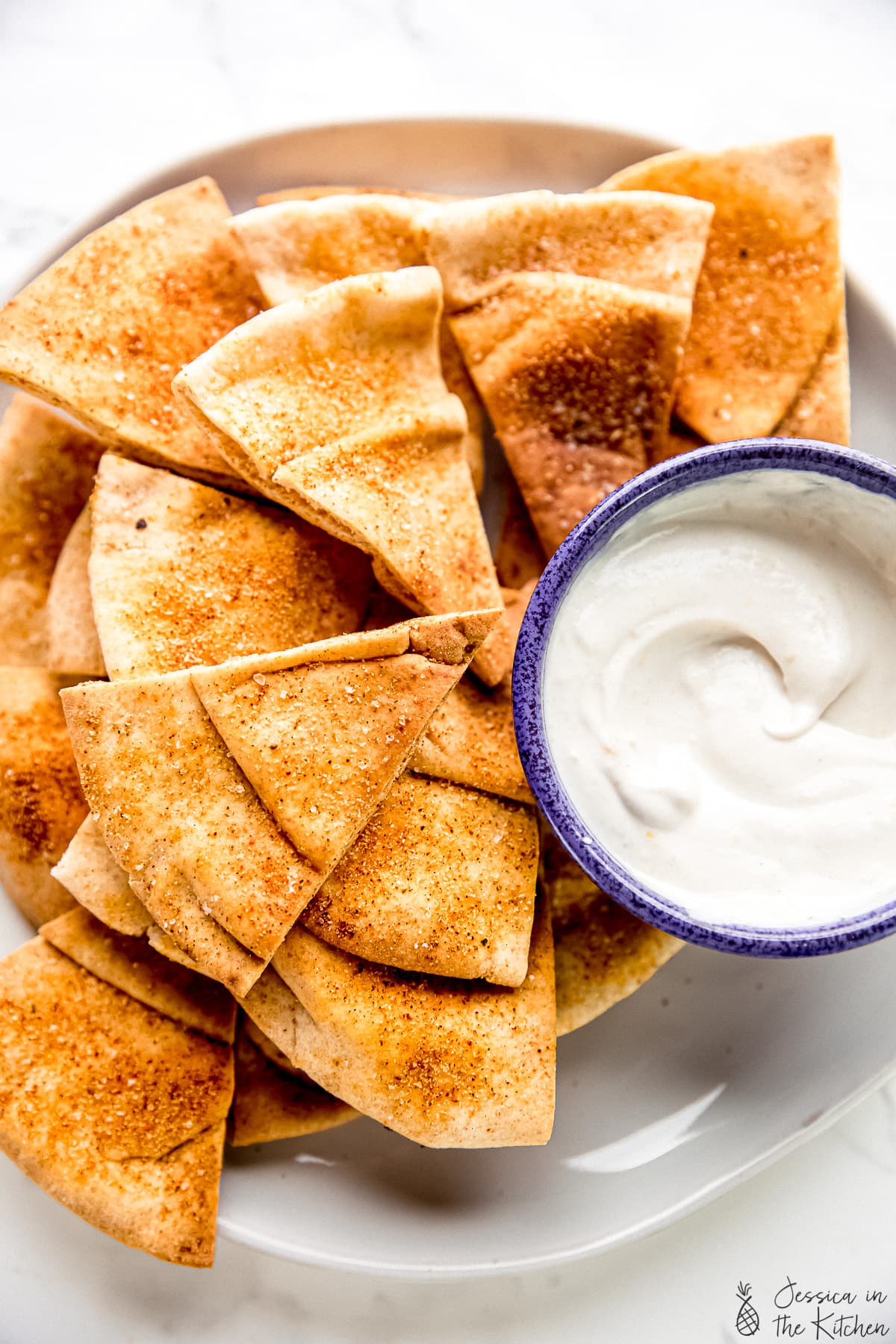 Homemade pita chips in a plate stacked with a dip beside it.