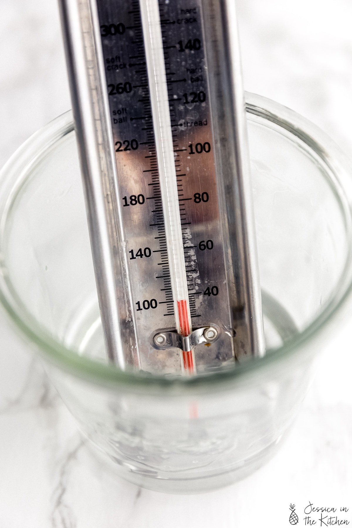 A candy thermometer in a bowl of warm water at 100 degrees Fahrenheit or 40 degrees Celsius. 