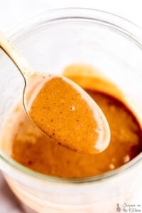 Thai peanut sauce in a gold spoon over a jar.