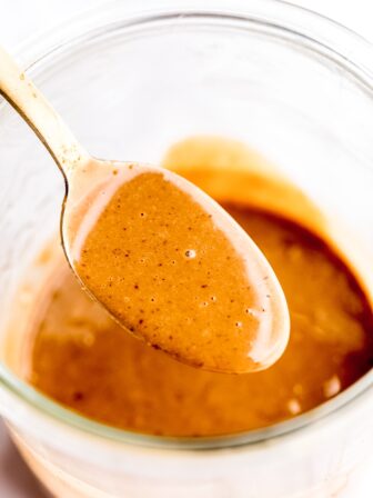 Thai peanut sauce in a gold spoon over a jar.