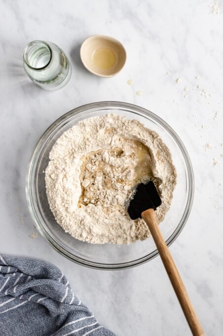 flour, oil yeast and other pizza dough ingredients in a bowl with a spatula