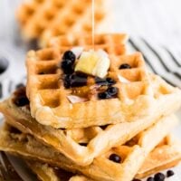 vegan waffles stacked on top of each other with maple syrup drizzle on top