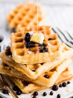 vegan waffles stacked on top of each other with maple syrup drizzle on top