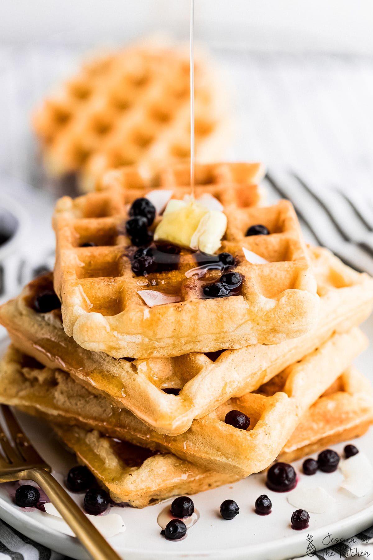 vegan waffles stacked on top of each other with maple syrup drizzle on top