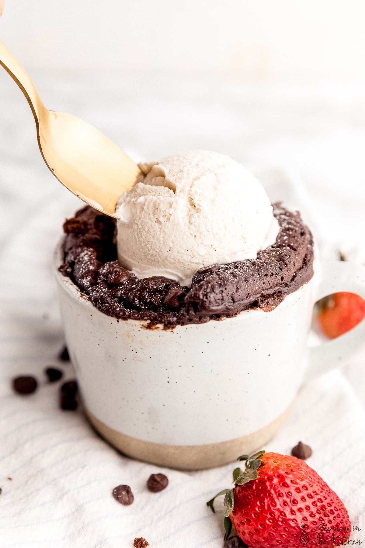 Close up photo of mug cake with a scoop of ice cream on top with spoon scooping some ice cream out.