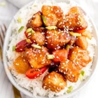 Sweet and sour tofu on white rice in a bowl with a fork beside it on a napkin.