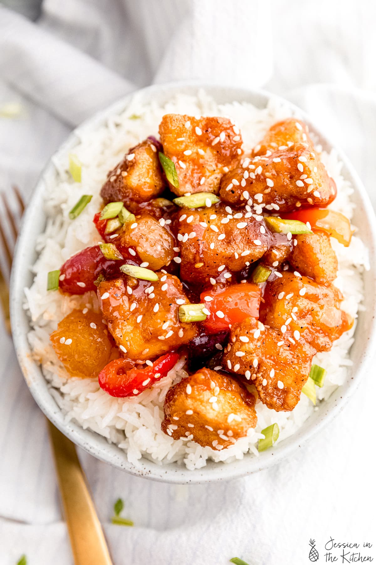 Sweet and sour tofu on white rice in a bowl with a fork beside it on a napkin.