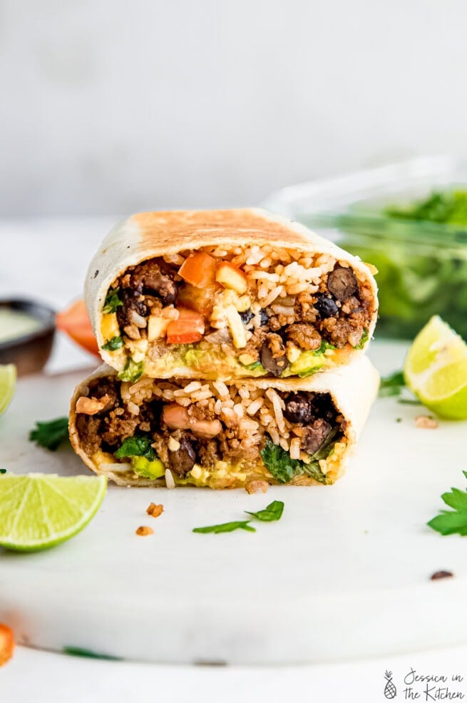 Stacked Vegan burrito on a white cutting board surrounded by lime, parsley and ingredients.