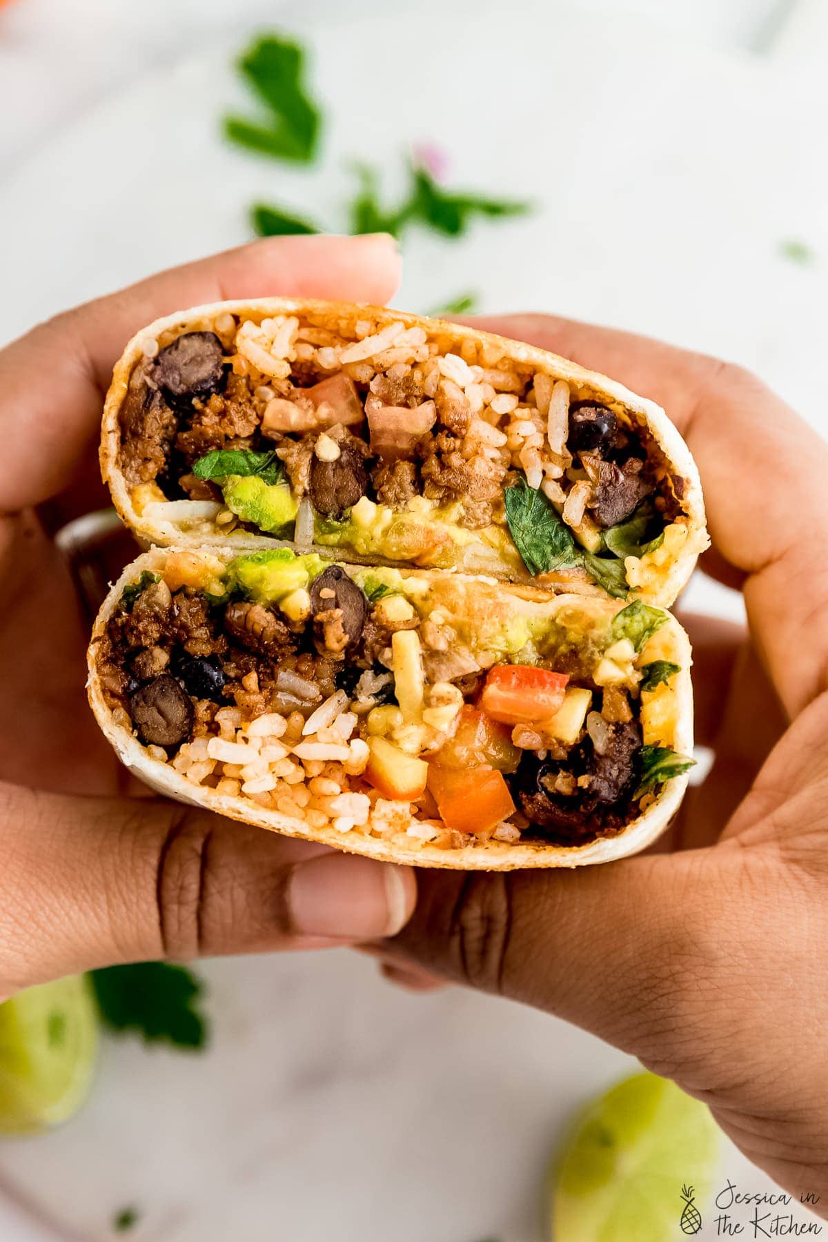 Hands holding vegan burrito that is cut in half.
