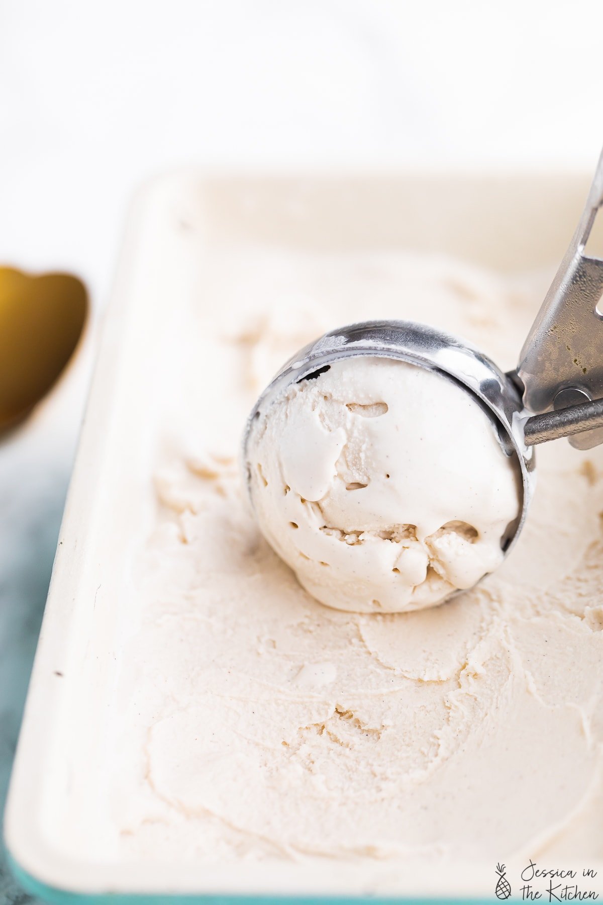 Ice cream in a scoop being scooped out of a large container of ice cream.