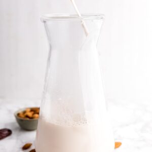 Almond milk being poured into a jar with raw almonds and dates surrounding it.