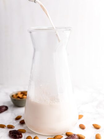 Almond milk being poured into a jar with raw almonds and dates surrounding it.