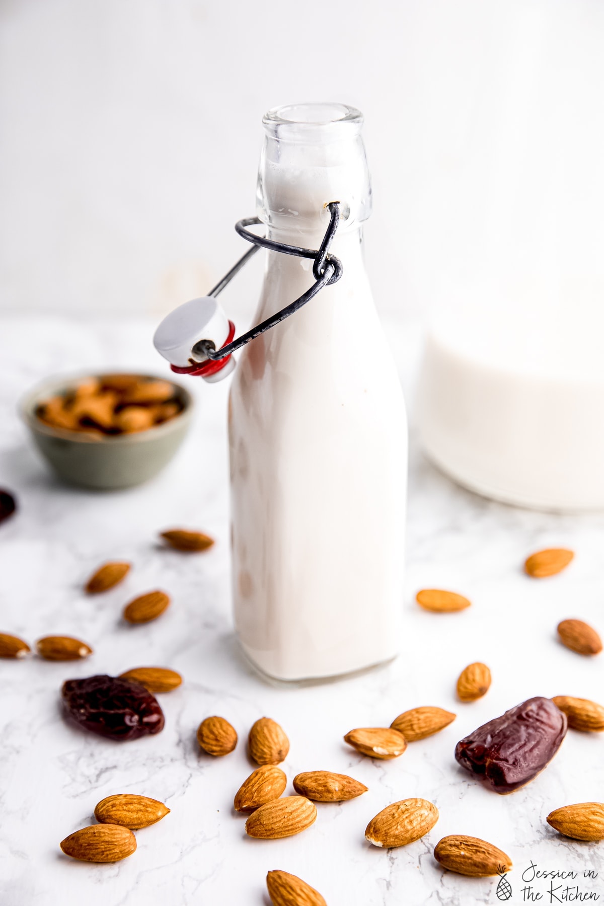 Almond milk in a milk jar surrounded by raw almonds and dates.