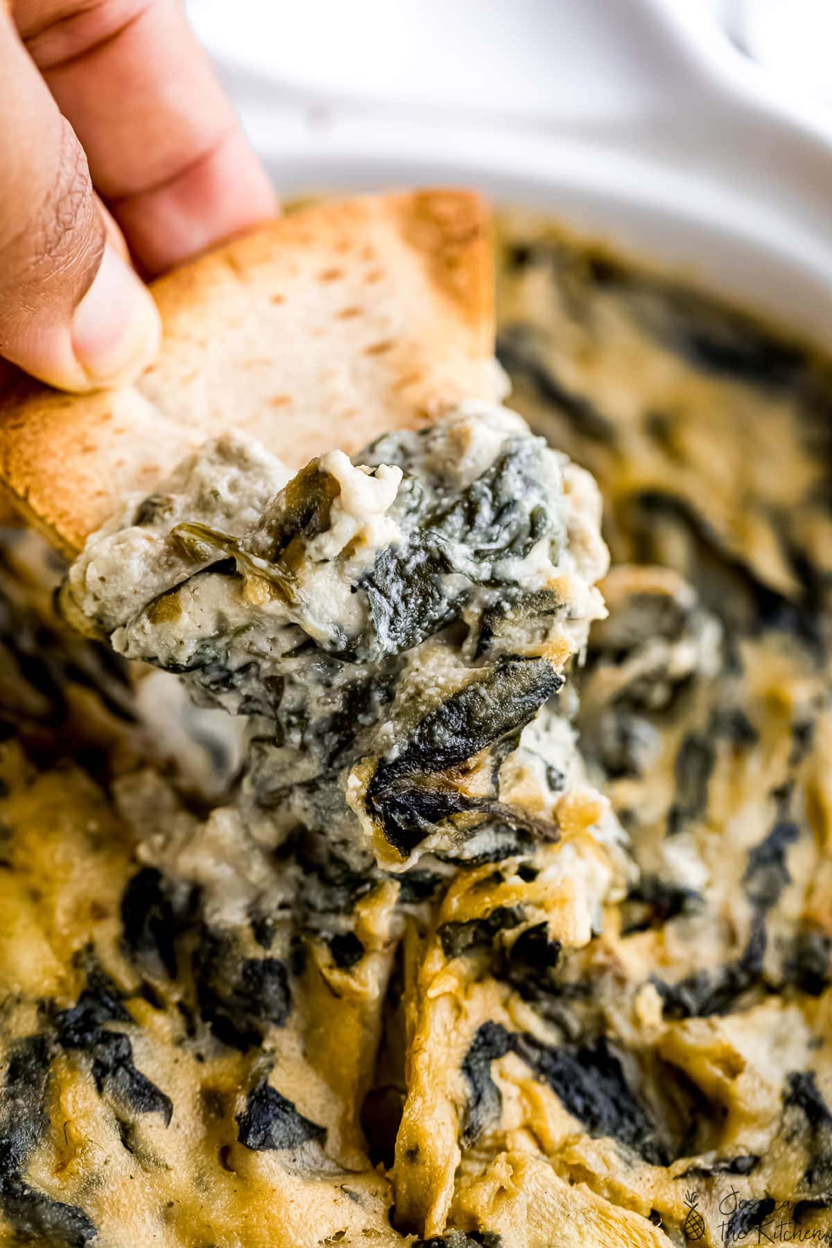 Close up shot of spinach artichoke dip on a pita chip.
