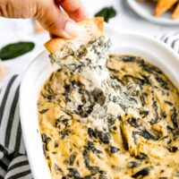 Photo of spinach artichoke dip being pulled up by a pita chip.