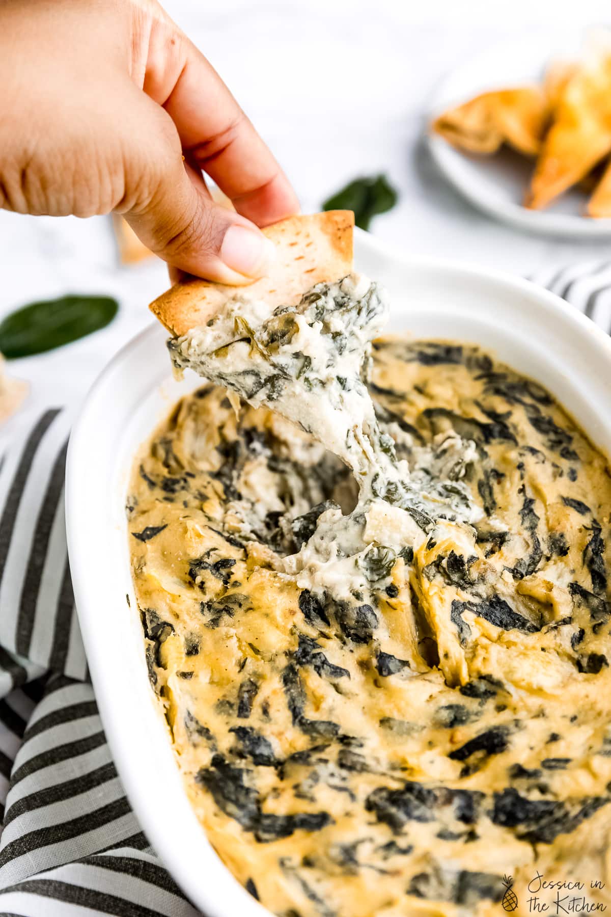 Photo of spinach artichoke dip being pulled up by a pita chip.