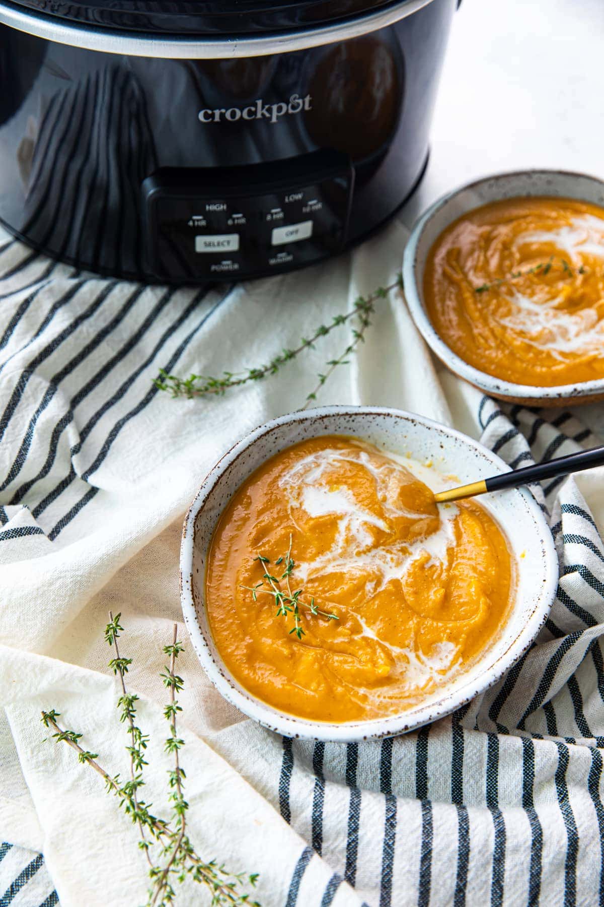 Vegan pumpkin soup in two bowls with slow cooker in background.